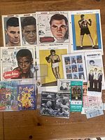 Overview photo showing assortment of boxing memorabilia on a wooden floor including magazines, stamps, tickets, and cards.