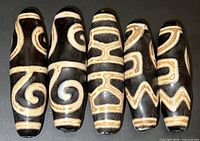 Front-facing view of five Tibetan Dzi beads, showing detailed patterns and overall color.