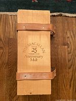 Top closed view of wooden box with leather straps, gold embossed text The Macallan 25 Year Anniversary Malt