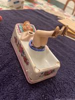 Angle showing full porcelain ashtray with reclining girl figure, legs raised, floral decorations