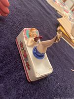 Side angle showing reclining woman with raised legs and red fan, floral side decoration, cigarette rests on ashtray