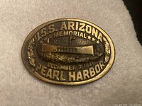 Front side of commemorative bronze belt buckle showing USS Arizona relief and text.