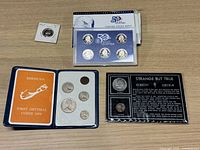 Top view of all items in the lot on a table showing the Bermuda decimal coin set, US quarters proof set, Kennedy and Lincoln fact cards with coins, and a 1969 S proof Jefferson nickel in holder.