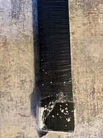 End of one black shelf wrapped in plastic with foam protection at the end