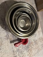 Top view of 6 nested stainless steel mixing bowls with the smallest in the center and the largest on the outside, placed on a textured surface.