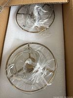 Two unopened crystal chandelier fixtures in gold frames inside a box with foam padding.