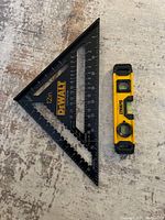 Top view of DeWalt black speed square and yellow magnetic level side by side on the floor.