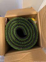Rolled green artificial turf mat seen inside original box.