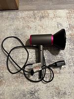 Hair dryer lying flat on carpet showing side profile and diffuser attachment on nozzle.