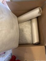 View of square and cylindrical cushions in original cardboard box with plastic protective wrapping.