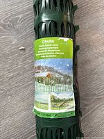 Roll of green plastic barrier fence with label showing product information in multiple languages and images of usage outside.