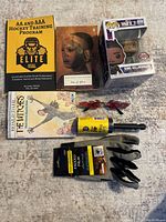 Overview of lot items including 3 books, King Killmonger Pop figure, two pairs of sunglasses, lint roller, and utility gloves on carpet.