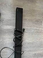 Full view of the Samsung soundbar with power cord visibly wrapped around it, laid on a wooden floor.