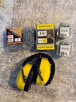 Overview of five boxes/packages of screws including 2-inch screws, 1 1/4 inch roofing nails, two small boxes of screws, and one pair of yellow and black noise cancellation ear muffs.