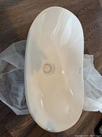 Top-down view of glossy white oval bathroom sink showing smooth surface, drain hole, and size perspective.