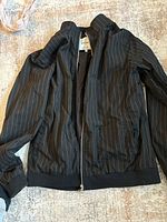 Full view of a black lightweight men's jacket with thin vertical stripes, zip-up front, ribbed cuffs and hem.