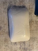Full view of the boxed Tempur-Pedic pillow showing its contoured shape and textured white cover inside plastic packaging.
