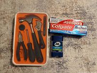 Full view of the mini tool kit package with hammer, pliers, wrench, and screwdriver alongside Colgate toothpaste and Right Guard deodorant.