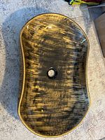 Top-down view of the oval vessel sink showing the black and gold marble-like pattern, oval shape, and central drain hole.