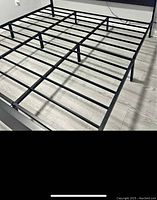 Black metal king size bed frame with horizontal and vertical support bars to hold mattress, photographed on light wood floor.