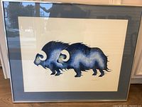 Full view of framed art print depicting two stylized musk-ox in dark blue against off-white background with mat and frame.