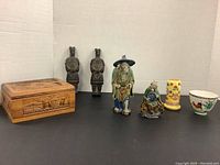 All lot items arranged on white background showing porcelain and terracotta figurines, toothpick holder, bowl, and carved wooden box.