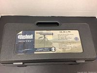 Closed black molded plastic carrying case with Bushnell Sentry spotting scope label and product features.