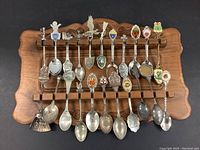 Front view of approx 20 collector souvenir spoons on carved wooden display rack