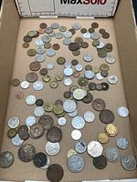 Top-down photo showing the full collection of assorted foreign coins laid out in a box, exhibiting a wide variety in size, color, and design.