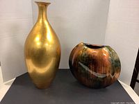 Two composite vases, one tall gold coloured with polished finish and one round multicolour (gold, green, orange) glossy vase.