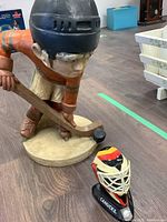 Composite No 7 hockey player statue with orange jersey, black helmet, holding hockey stick and puck, next to a Canucks model hockey helmet.