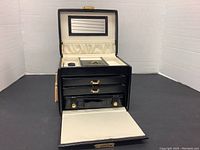 Open view of the jewelry box showing upper compartment with ring slots, mirror inside lid, and light cream lining.