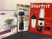 Photo showing Hamilton Beach personal blender in box, Mastrad kitchen scale new in box, and Starfrit personal blender box with accessories displayed.