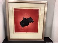 Full frontal image of framed raven silhouette artwork by Ochs against red background.