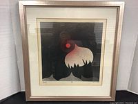 Front view of the framed artwork showing the raven and sun image with a pinkish silver frame.