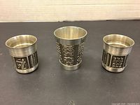 Front view of three pewter cups showing decorative relief panels and sizes