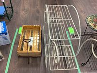 Photo of white metal wagon-style plant stand with two levels, placed on wooden floor next to a wooden pull cart and floral tabletop.