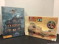 Two unopened 3D puzzles side by side: Storm Croft Manor (1000 pieces) and Great Wall of China (Puzz 3D by Wrebbit).
