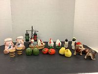 Full view of all salt and pepper shakers lined up on a black surface against white backdrop showing pigs, lanterns, poultry, penguins, and animals.