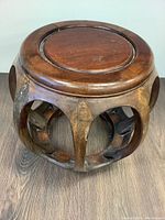 Wood round stool viewed from front-left angle showing carved open sides and solid top with recessed center ring.