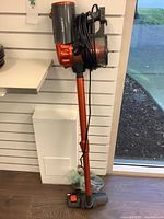 Full view of the Iwoly stick vacuum standing upright showing handle, dust container, and power cord wrapped around the handle.