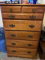 Front view of the dresser showing all five drawers with metal handles, clean top surface with some items on it, and visible wear on lower edges.