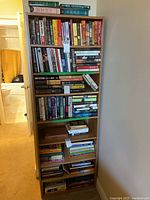 Front view of a tall particle board bookshelf with seven shelves filled with books. Shows wear on the wood grain finish.