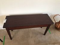 Full view of the rectangular antique piano bench showing its overall shape and condition.