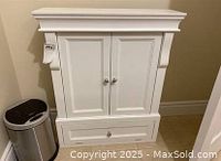 Front view of white bathroom cabinet with two paneled doors, bottom drawer, and sensor garbage bin beside it.
