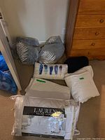 Lot showing gray pillows with leaf pattern, black throw, feather design accent pillow, white quilted pillow, and Ralph Lauren feather bed pillow in packaging.