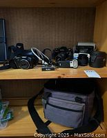 Shelf with Konica Autoreflex TC camera, Canon Powershot camera, Braun flash unit, Kenko filter, cables, and carrying case below shelf