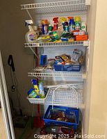 Shelving unit with assorted cleaning and household items including spray bottles, gloves, sponges, lightbulbs, and bins with additional supplies. Swiffer mop visible in corner.