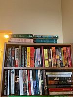 Wide shot of the bookshelf featuring multiple fiction novels tightly arranged, including several James Patterson books, thrillers, and contemporary fiction.