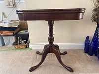 Front view of the antique wooden pedestal games table showing turned central support and curved legs.